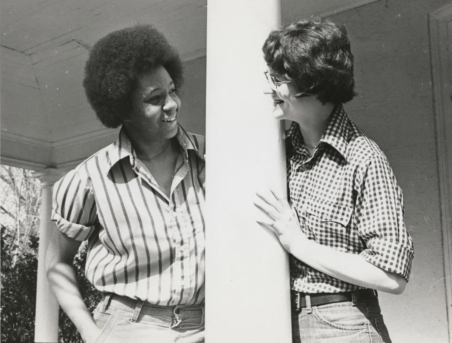 Two women are leaning on a pillar, smiling at each other. Two women are leaning on a pillar, smiling at each other.