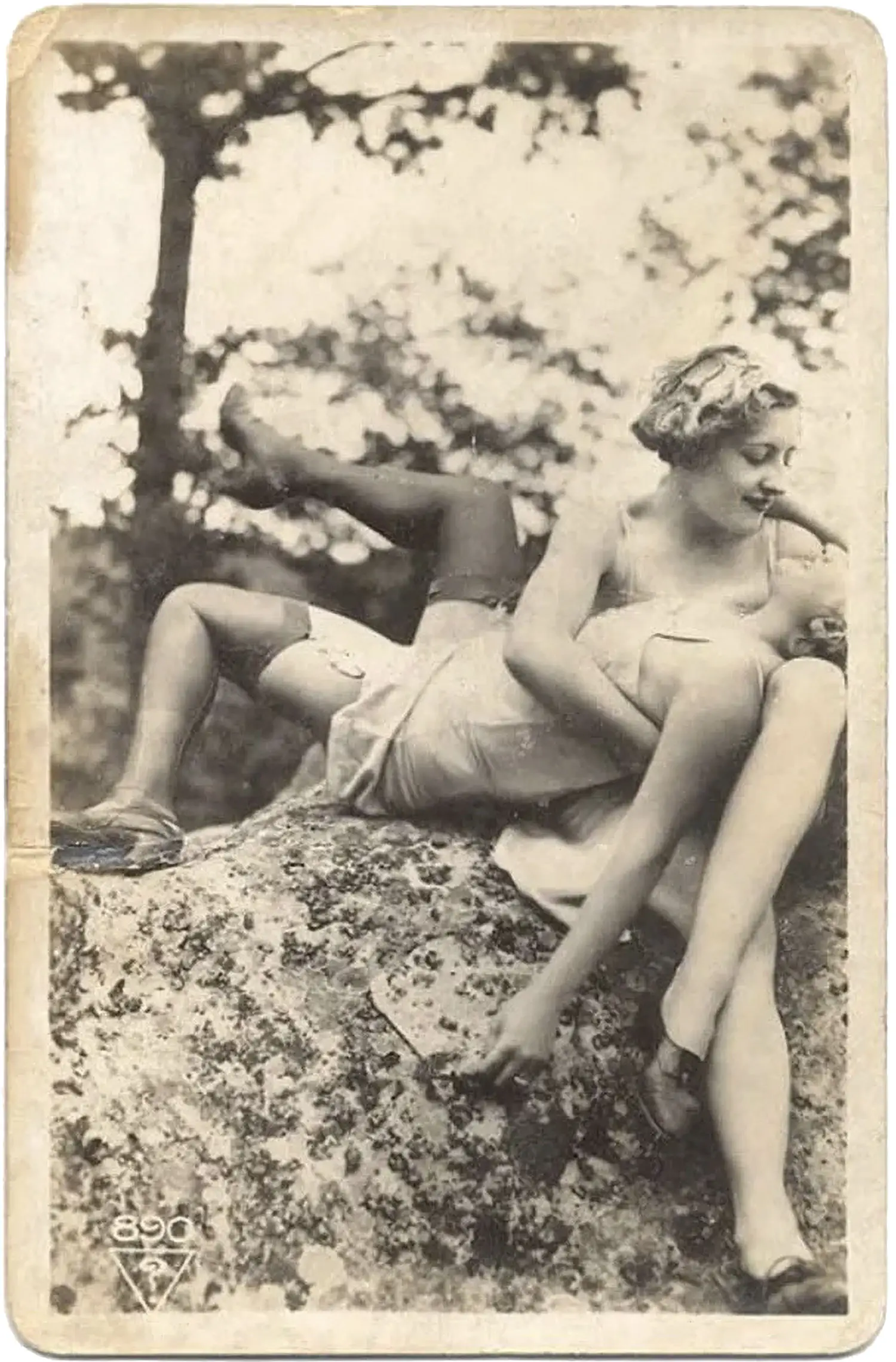 A weathered photograph of two women relaxing atop a large rock outdoors. One woman lies on her back, held by the other, who looks down at her face, smiling. A weathered photograph of two women relaxing atop a large rock outdoors. One woman lies on her back, held by the other, who looks down at her face, smiling.
